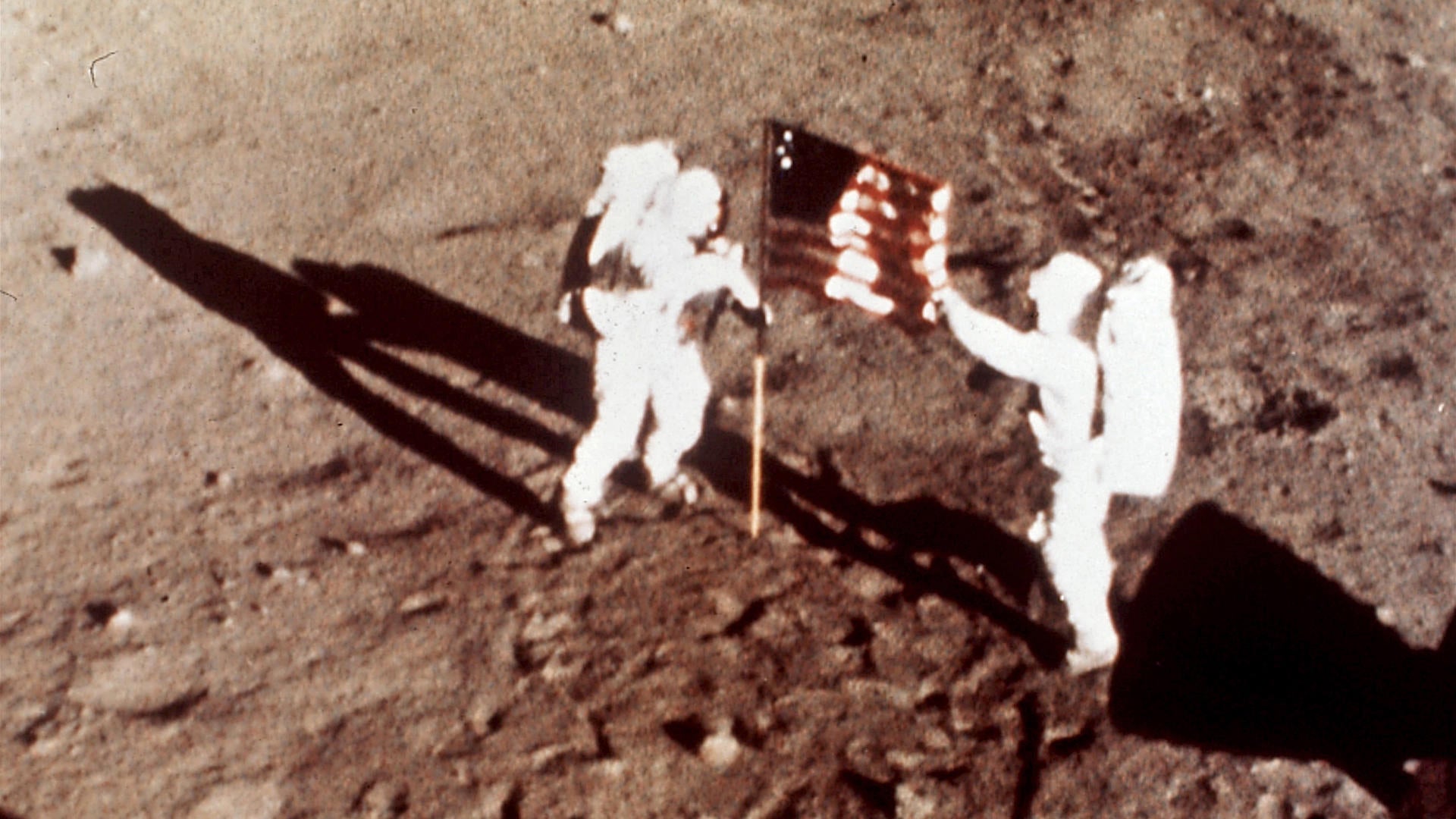 neil armstrong on the moon holding flag