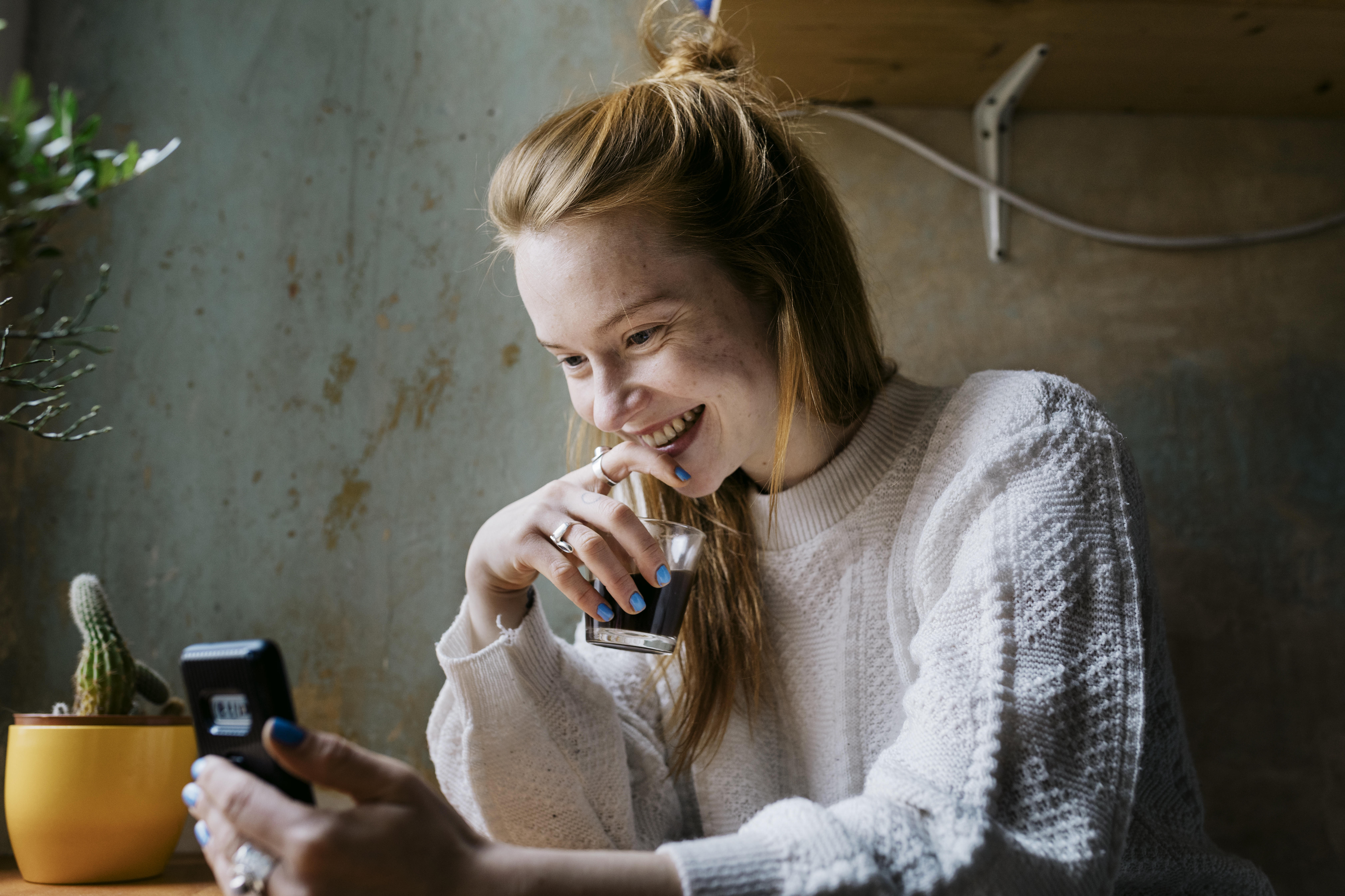 A girl relaxing with a coffee in her living room at home and smiling while video calling her partner with her smartphone. 