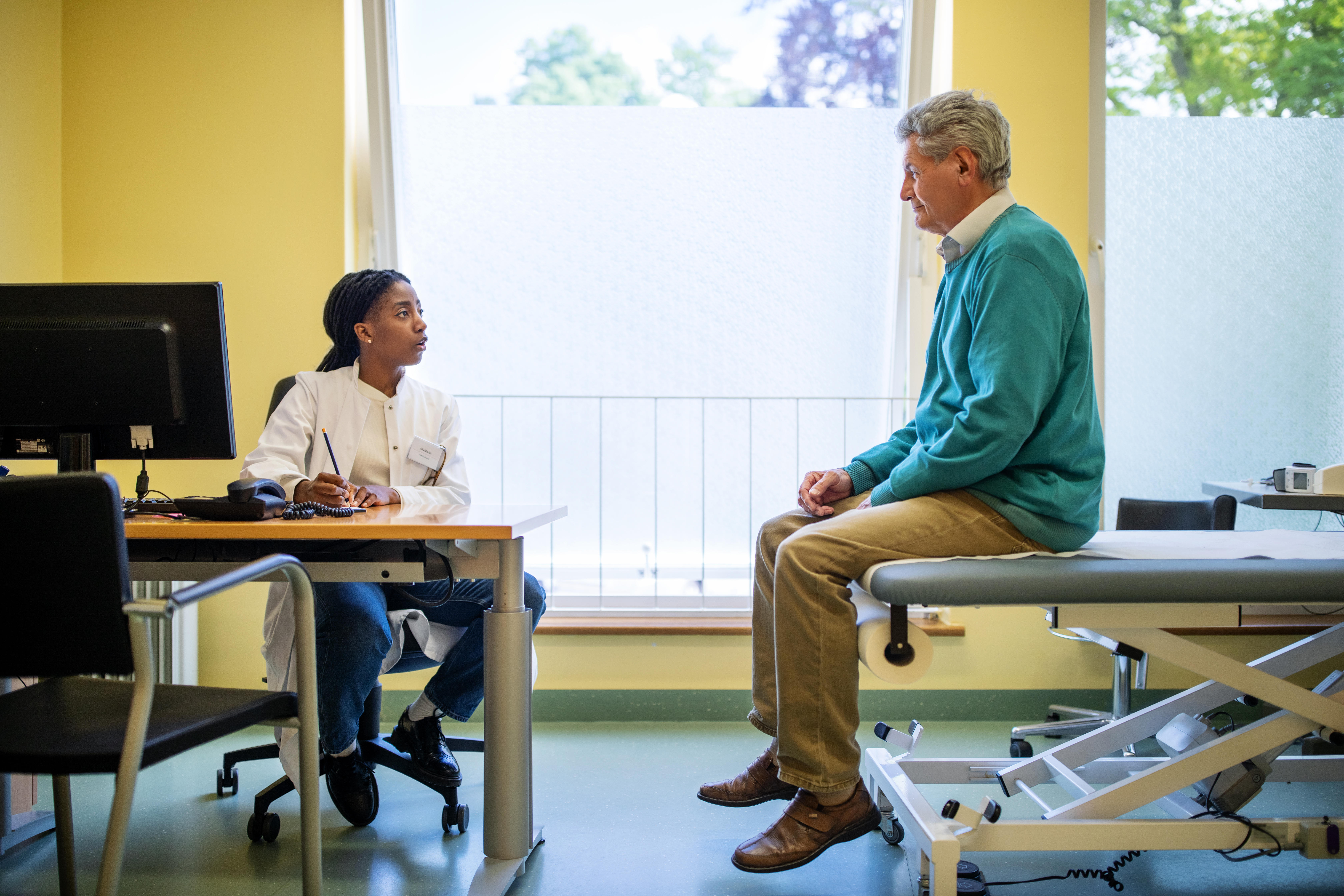 Doctor sitting in her office talking to an older male patient. 