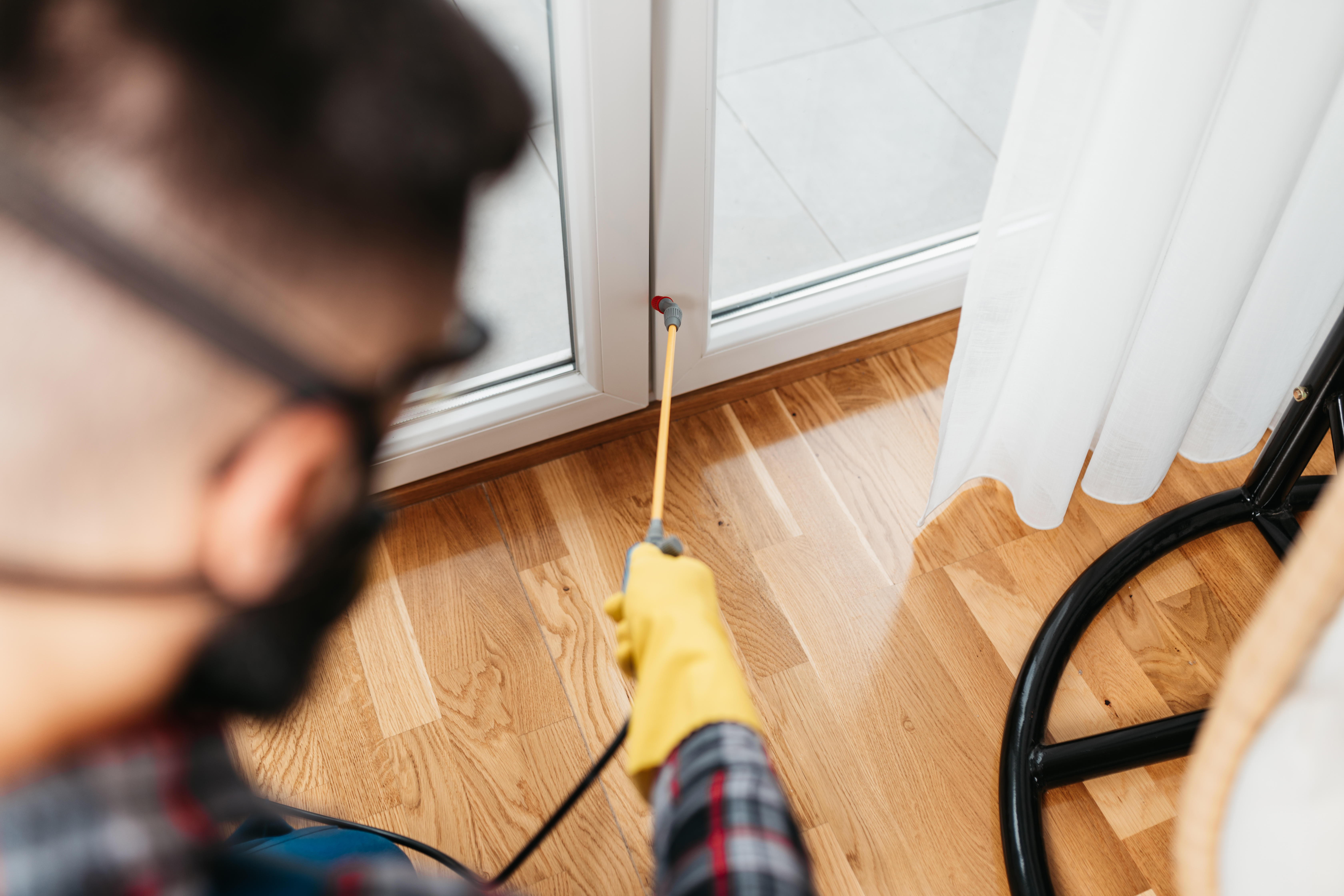 Pest control professional in protective workwear carefully sprays pesticide in an apartment. 