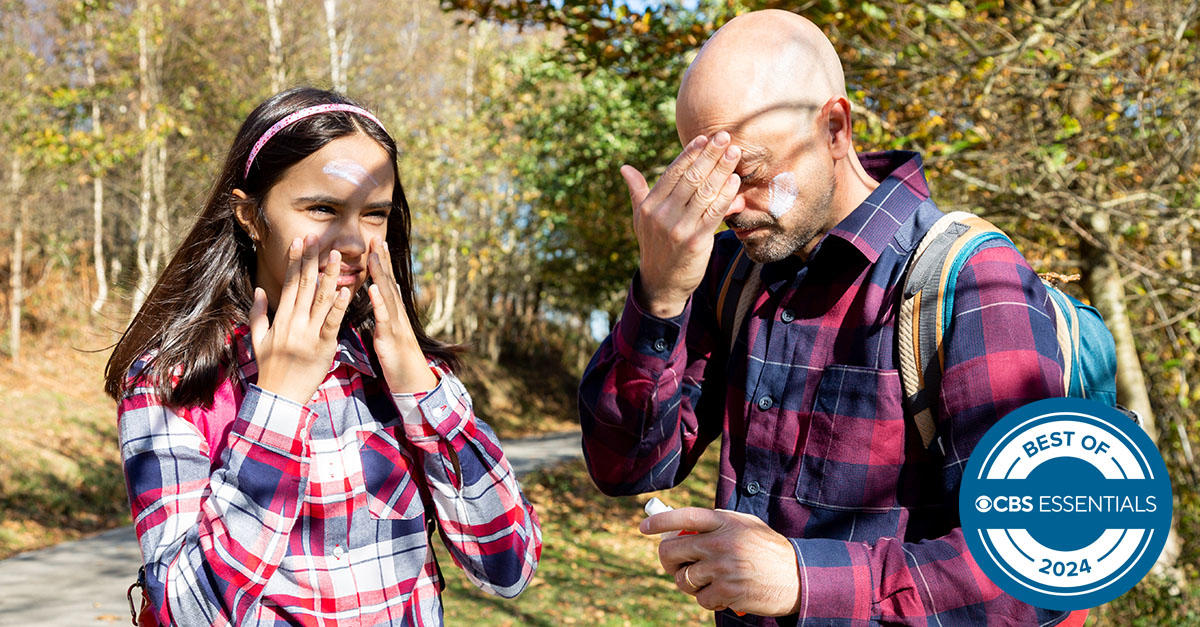 Father and teenage daughter applying sunscreen lotion before hiking in autumn 