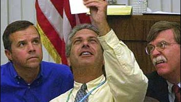 Judge Charles Burton, chairman of the Palm Beach County canvassing board holds up the last ballot the board was able to consider in the manual recount of ballots as Democratic lawyer Mark White, left, and Republican lawyer John Bolton watch at the Palm Be 