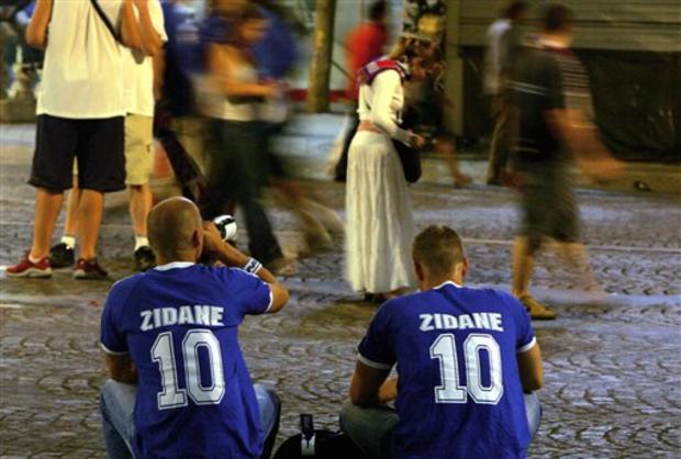 Two supporters, wearing jerseys with the name of French soccer team captain Zinedine Zidane, drink and sit on the Champs Elysees 