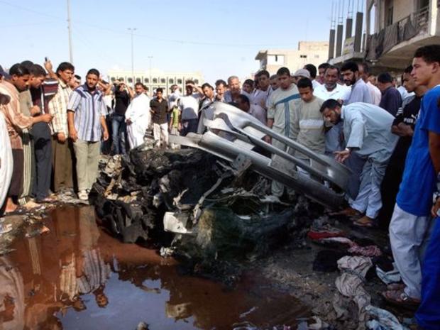 Local Iraqis gather around the wreckage of a car bomb attack 