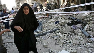 An Iraqi woman walks past the site of Wednesday's car bomb explosion, in Baghdad, Iraq 