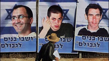 A man looks at banners of captured Israeli soldiers Ehud Goldwasser, left, Gilad Shalit, center, and Eldad Regev, right, placed in protest outside the Prime Minister's office in Jerusalem 