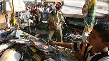 A boy checks burnt out posters of radical Shiite cleric Muqtada al-Sadr at a stand destroyed by a car bomb 