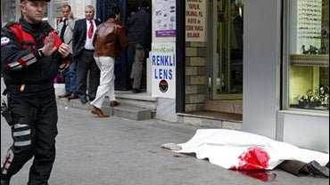 A Turkish policeman walks near the covered body of the journalist Hrant Dink at right, in Istanbul, Turkey, Friday, Jan. 19, 2007. 