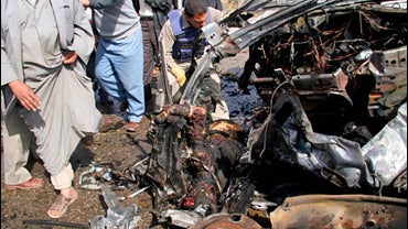 Iraqis gather to inspect human remains inside a wreck of a car destroyed in a car bomb attack in Najaf 
