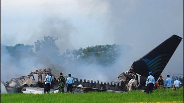 Investigators look at the still smouldering wreckage of a Garuda airlines Boeing 737-400 which burst into flames as it landed at Yogyakarta international airport 