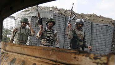 Iraqi soldiers celebrate next to a wrecked car that was driven by a suicide bomber in Baghdad's Yarmuk neighborhood 