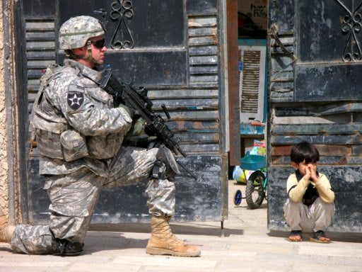 Iraqi kid squats by a US soldier on a patrol in the Shiite enclave of Sadr City in Baghdad, Monday, March 19, 2007. 