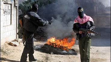 Masked Palestinian militants stand next to burning tires creating smoke to block Israeli aircrafts' view, during an Israeli army operation in the southern Gaza Strip town of Khan Younis, Thursday, Jan. 3, 2008. 