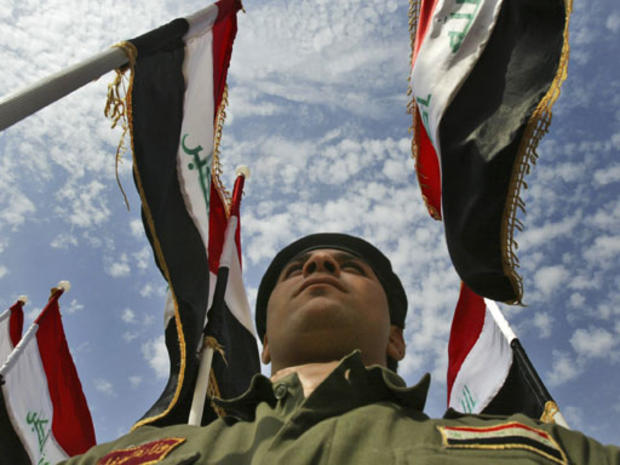 Iraqi police graduate stands at attention as national flags flutter above him, during a graduation ceremony in Baghdad, Iraq 