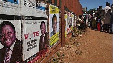 People queue for food in front of election posters with portraits of main opposition leader Morgan Tsvangirai, left, in Harare, Zimbabwe Friday, April 4,2008. 