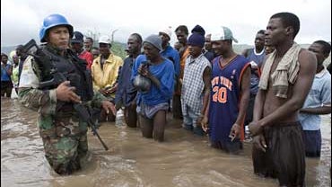 A Bolivian peacekeeper, left, stands on an area flooded by heavy rains from Tropical Storm Hanna next to residents in Savan Desole, Haiti 
