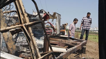 Palestinians walk near a burnt out vehicles after gunmen clashed with Israeli forces near the Nahal Oz crossing east of Gaza City, Monday, June 8, 2009. 