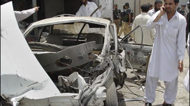 Local residents stand around a damaged car at the site of a bomb explosion in a market in Dera Ismail Khan, Pakistan on Sunday, June 14, 2009. 
