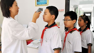 A medical worker checks the temperature of students to identify symptoms of the H1N1 flu on the first day of their new semester at a middle school in Shanghai, China, Tuesday, 1 September 2009. 