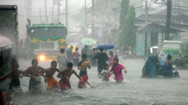 People wade through a flooded street passing stalled vehicles Saturday, Sept. 26, 2009 in suburban Malabon City north of Manila, Philippines. Non-stop overnight rain from tropical storm Ketsana has caused massive flooding in the city. 