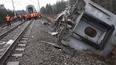 Railroad workers stand next to a damaged coach at the site of a train derailment near the town of Uglovka, some 250 miles northwest of Moscow, Russia, Saturday, Nov. 28, 2009. 