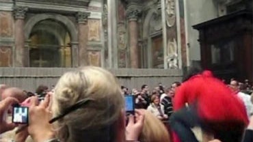 In this image made from amateur video obtained by APTN, an unidentified woman, right, jumps over the barricade towards Pope Benedict XVI as he walks down the main aisle to begin Christmas Eve Mass in St. Peter's Basilica in Vatican City on Thursday, Dec.  
