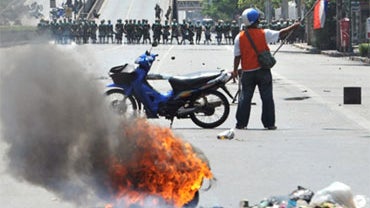A demonstrator supporting former Thai Prime Minister Thaksin Shinawatra holds a flag after burning a tire in Bangkok on May 14, 2010, in view of a line of government troops. 