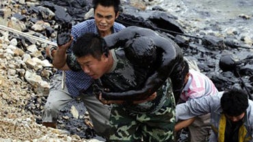 In this photo released by Greenpeace, a firefighter who was submerged in thick oil during an attempt to fix an underwater pump is brought ashore by his colleagues in Dalian, China on Tuesday, July 20, 2010. Crude oil started pouring into the Yellow Sea of 
