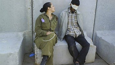 Israeli army soldier poses in front of blindfolded men identified in the Israeli media as Palestinian prisoners. 