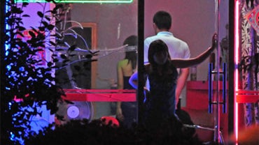 A woman awaits customers from the doorway of a neon-lit barber shop in Beijing on July 9, 2008. 