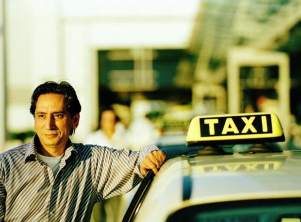 Driver leaning on taxi cab at airport 