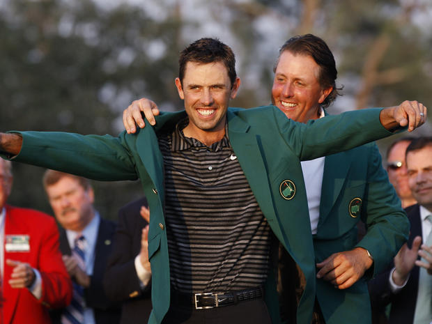 Former champion Phil Mickelson, back, helps Charl Schwartzel of South Africa with his green Masters jacket 