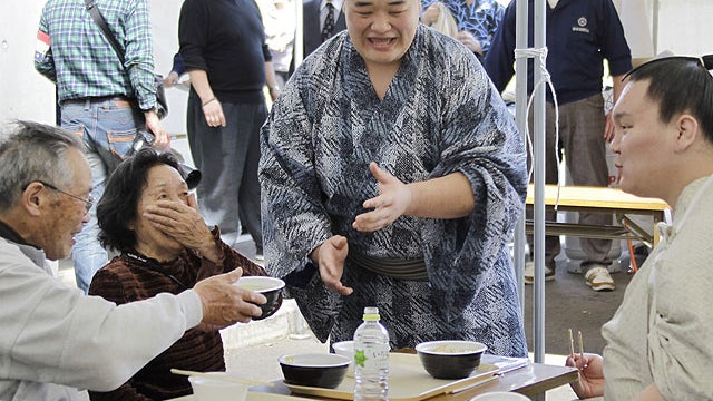 Mongolian sumo grand champion Hakuho, right, shares a light moment with a Japanese couple as he eats lunch which sumo wrestlers prepared for evacuees at an evacuation center at Ajinomoto Stadium in Tokyo, April 15, 2011.  