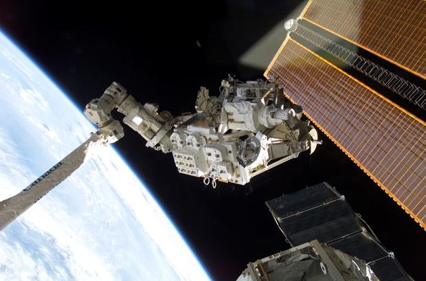 The Mobile Remote Servicer Base System (MBS) is seen here being moved by the Canadarm2 for installation on the International Space Station. Astronauts Peggy A. Whitson, Expedition Five flight engineer, and Carl E. Walz, Expedition Four flight engineer, at 