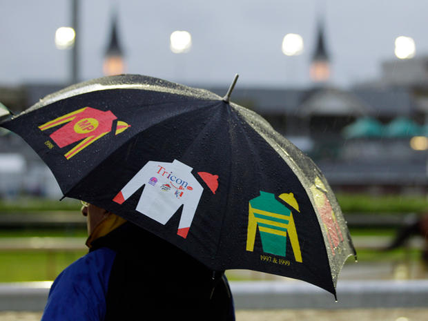 A fan holds an umbrella in the rain as he watches horses workout 
