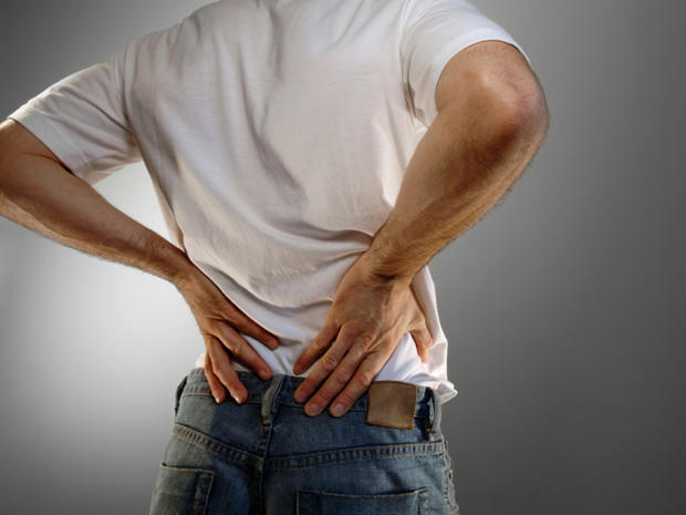 man in white shirt and jeans holding lower back in pain 