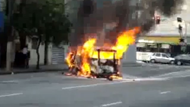 man walks by burning car 