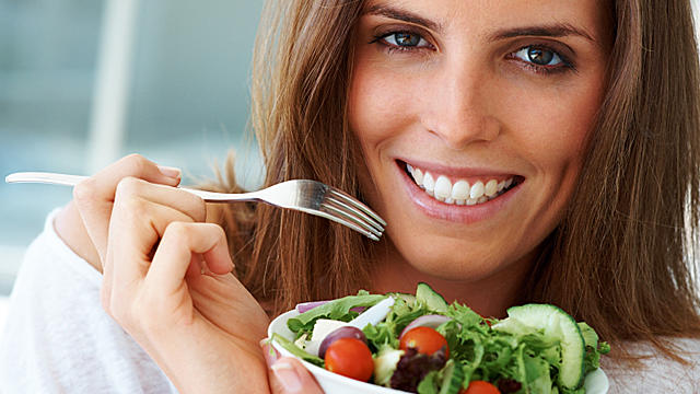 Close-up portrait of happy beautiful woman eating vegetable salad 