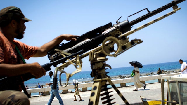 People walk to attend Friday prayers as a rebel fighter stands on guard in the rebel-held city of Benghazi, Libya, July 15, 2011. More than 30 nations, including the United States, declared that Libyan leader Muammar Qaddafi's regime is no longer legitima 