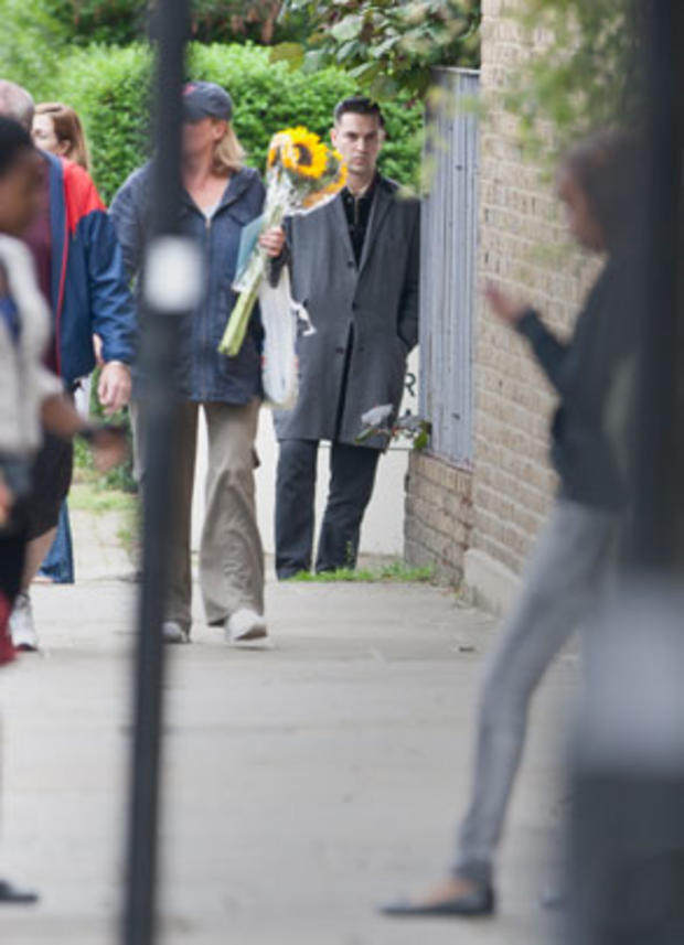 British singer and filmmaker Reg Traviss looks on as a member of the public passes to lay flowers near a police cordon by Camden Square, close to the home of British singer Amy Winehouse, who was found dead, July 23, 2011.  