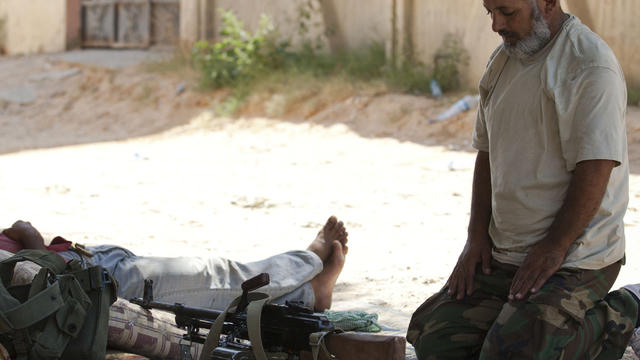 Libyan rebel prays with his weapons in the town of Zawiya 