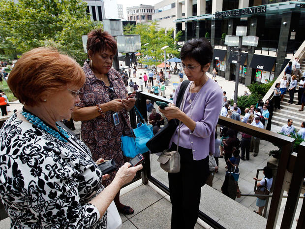 People check their phones as they wait outside of an office building after an earthquake was felt in Baltimore, Tuesday, Aug. 23, 2011.   