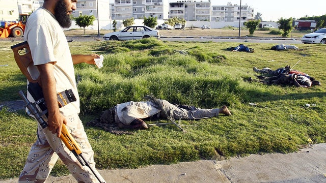 A Libyan rebel walks past bodies in Tripoli 