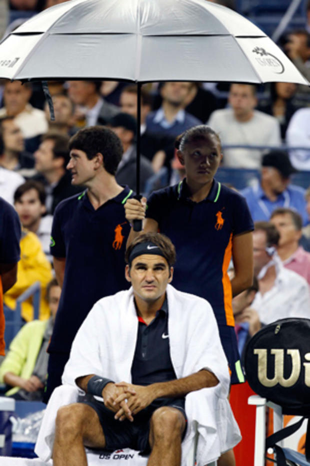 Roger Federer sits on a chair under an umbrella during a rain delay 