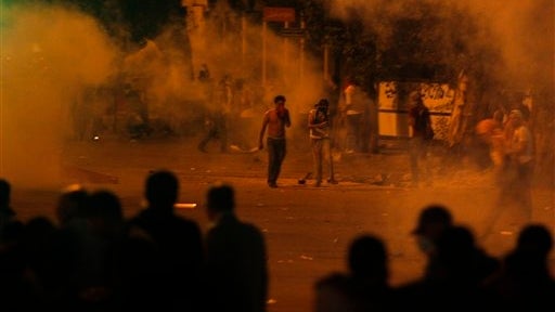 Protesters throw stones as tear gas is seen around them during clashes with Egyptian security forces next to building housing the Israeli embassy in Cairo early Saturday 