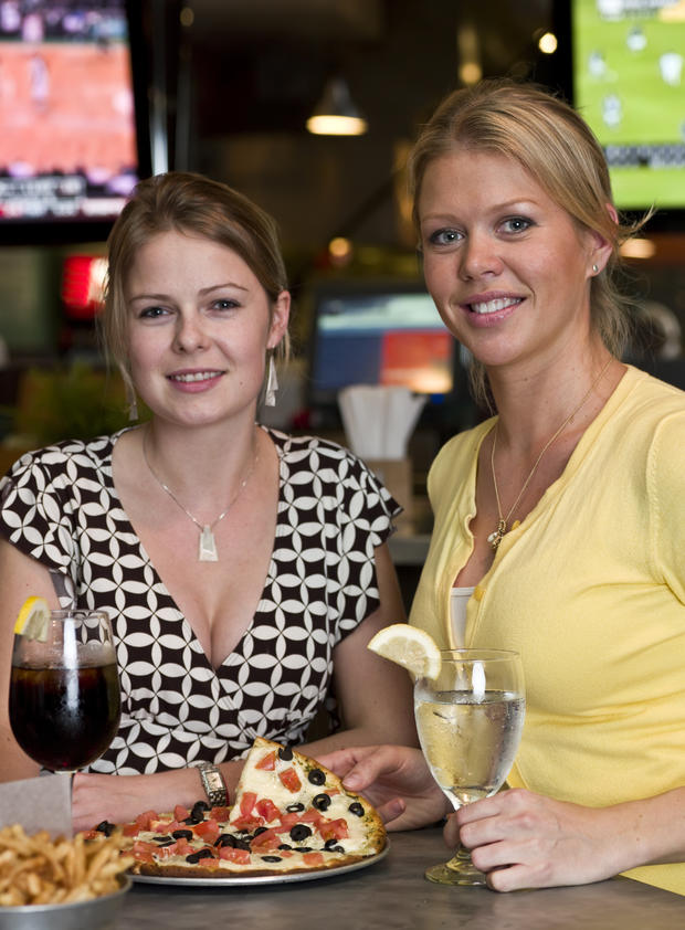 two-women-at-bar-smiling-and-eating-pizza-thinkstock 