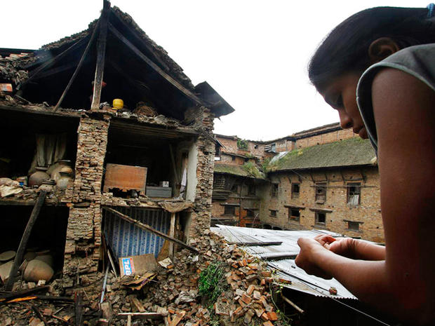 Nepalese woman looks out of a window at debris 
