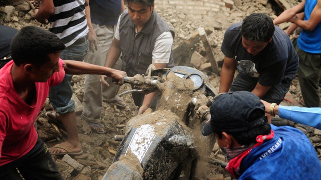 Nepalese people take out a motorbike buried under the debris  