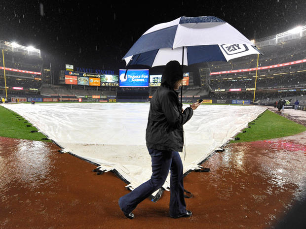 A person walks by holding an umbrella past a tarp-covered field 