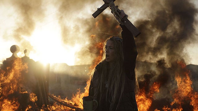 An Irish traveler resident holds up a cross for the media, in front of a burning barricade during evictions at the Dale Farm travellers site, near Basildon England, 30 miles east of London, Oct. 19, 2011.  
